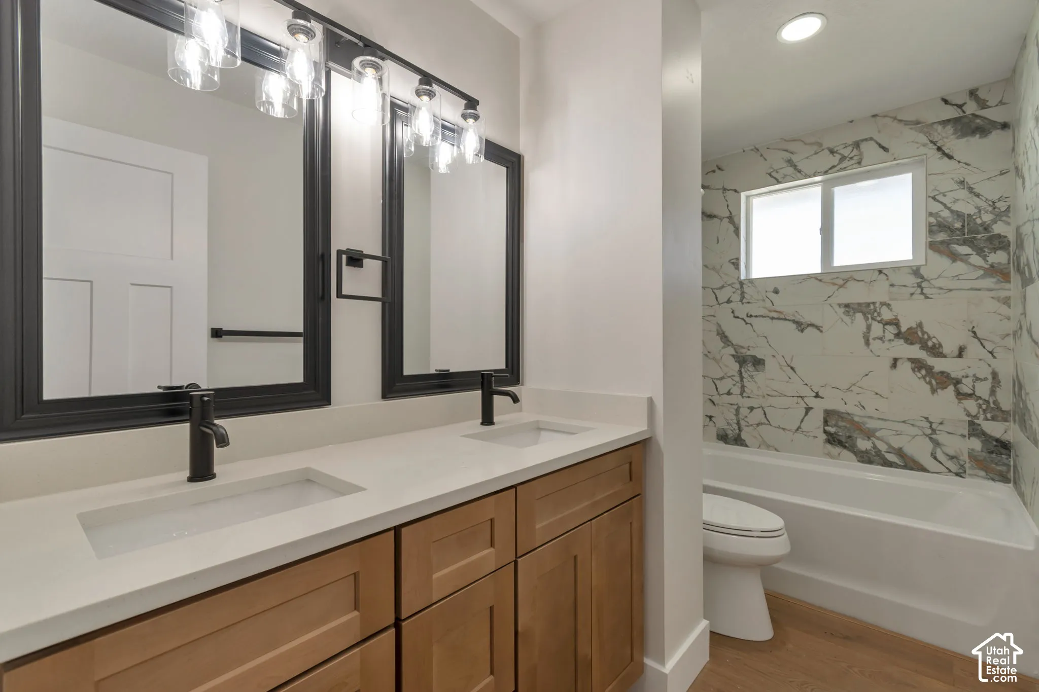 Dual vanity with light wood-finish cabinetry, integrated sinks, and matte black fixtures