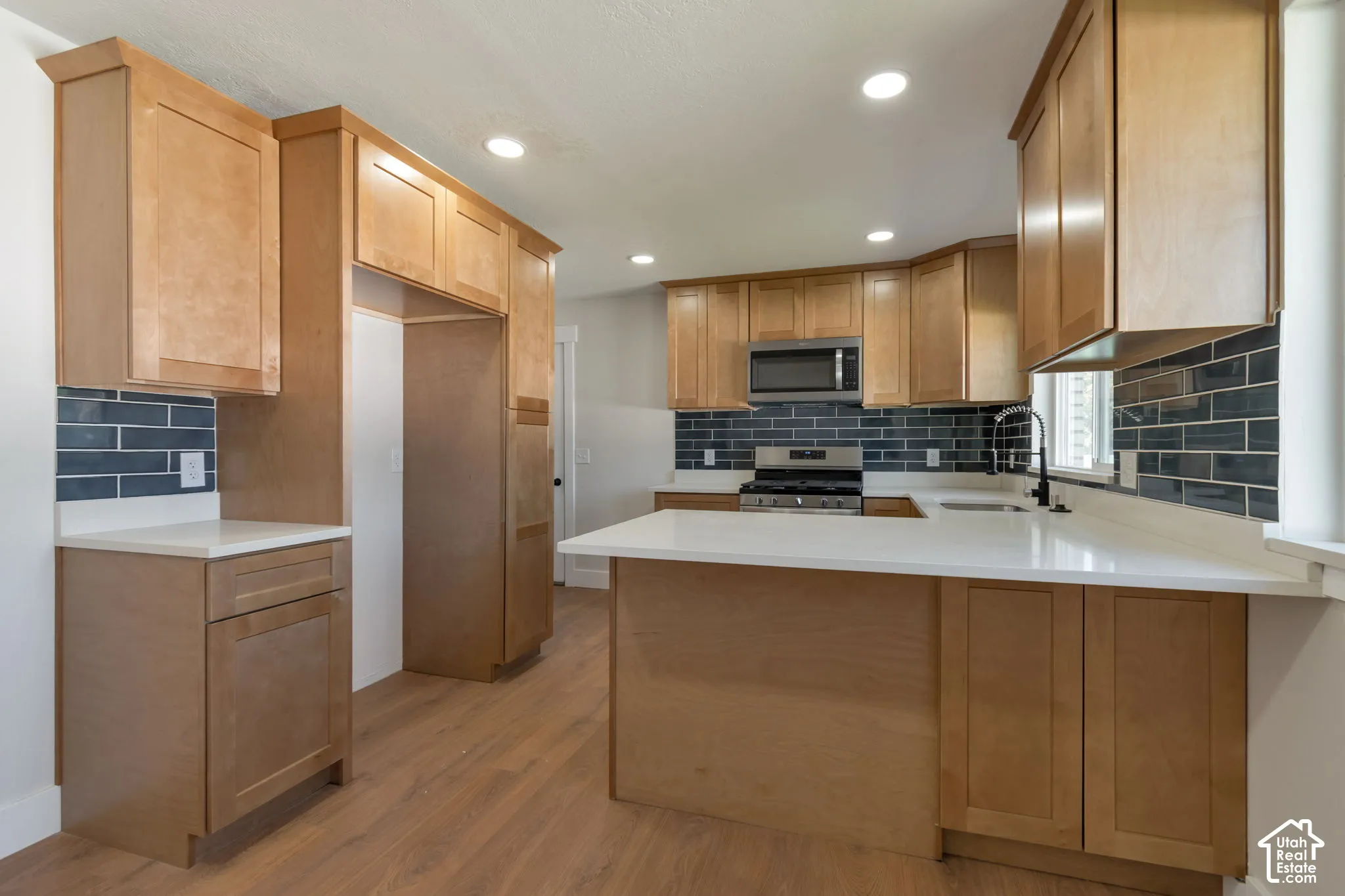Wood-finish flooring, recessed lighting, wood-finish cabinetry, light-toned countertops, and a subway tile backsplash