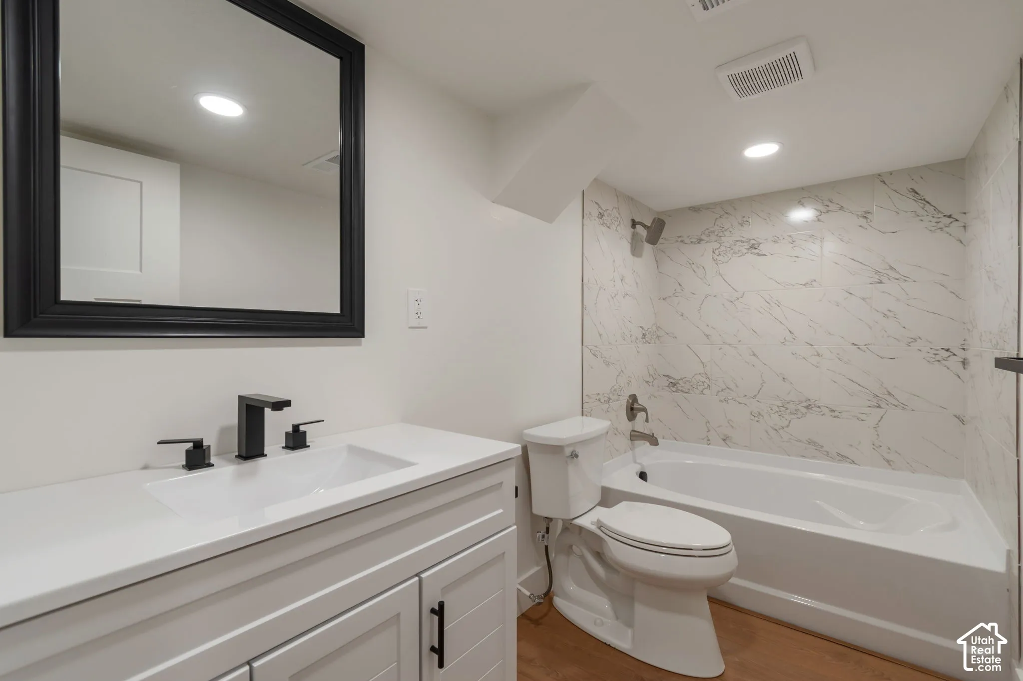 White vanity with matte black hardware and faucet, mounted mirror, and built-in bathtub with white and gray tiled surround