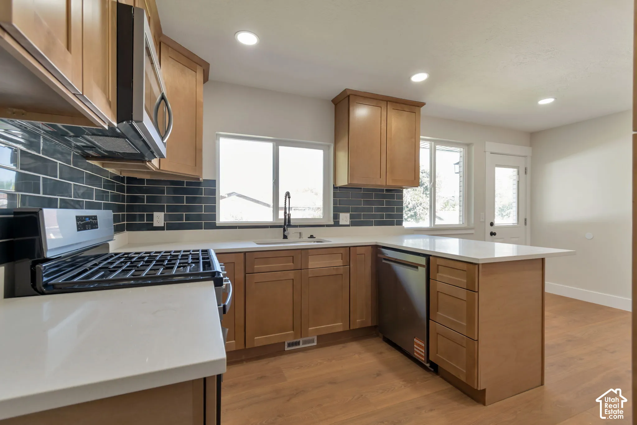Kitchen featuring light wood-finish cabinetry, white countertops, dark subway tile backsplash, and stainless steel appliances