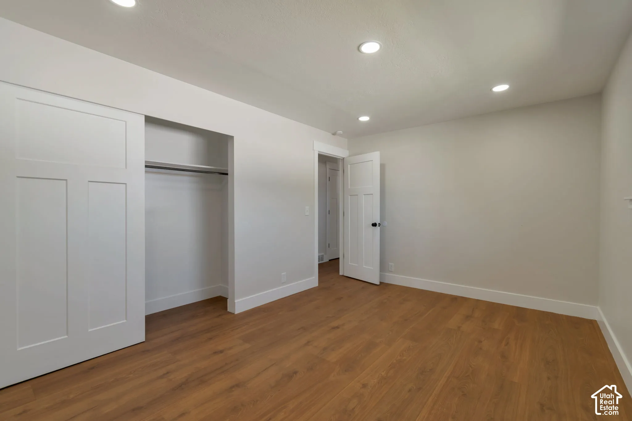 Recessed lighting, wood-finish flooring, white trim, solid core doors, and a closet with a built-in rod