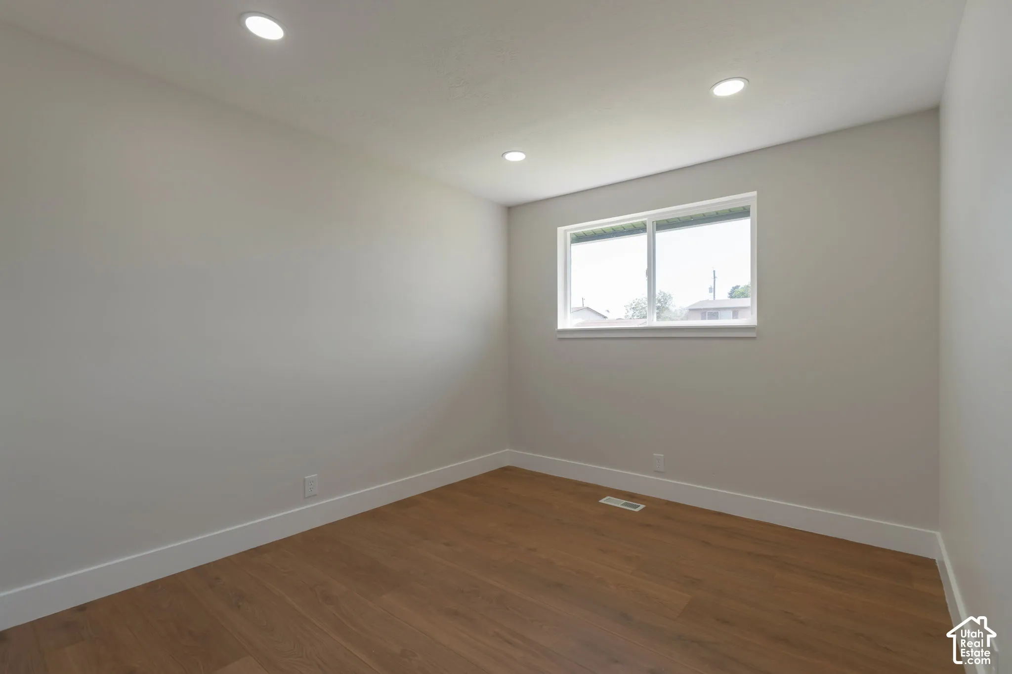 Recessed ceiling lighting, wood-finish flooring, white trim, and a window with white casing