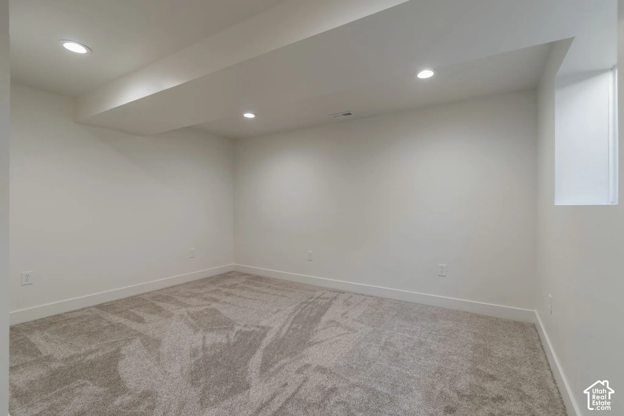 Recessed ceiling lighting, neutral carpeting, and a perimeter window