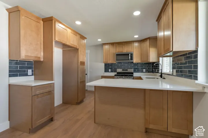 Wood-finish flooring, recessed lighting, wood-finish cabinetry, light-toned countertops, and a subway tile backsplash