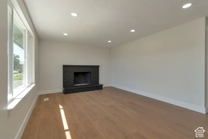 Spacious room with wood-finish flooring, a black brick fireplace, recessed lighting, and large windows