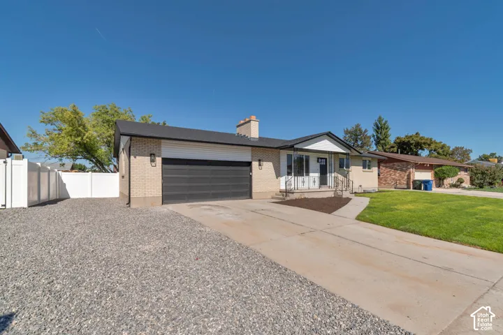 Brick-clad exterior with a dark asphalt shingle roof, integrated garage with a dark garage door, paved driveway, and a white fence