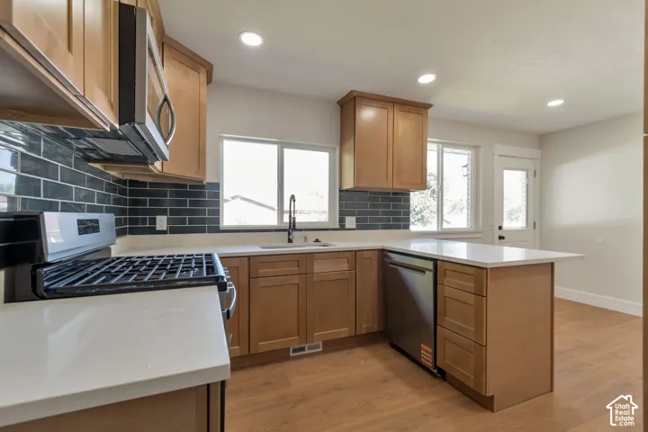 Kitchen featuring light wood-finish cabinetry, white countertops, dark subway tile backsplash, and stainless steel appliances