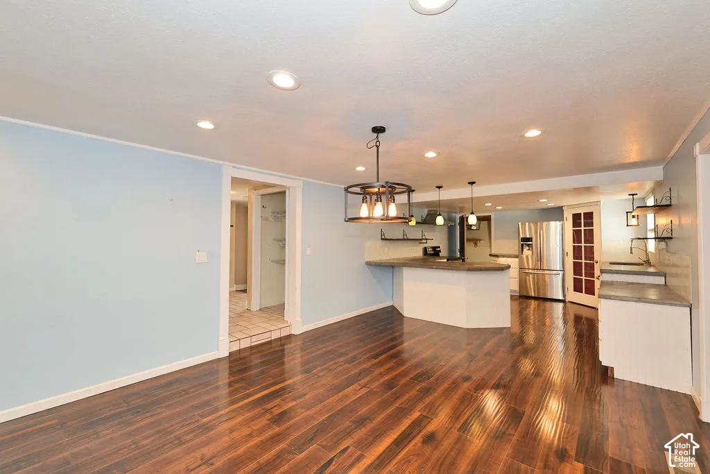 Recessed ceiling lighting, wood-finish flooring, island with countertop, stainless steel refrigerator, and glass-paneled door