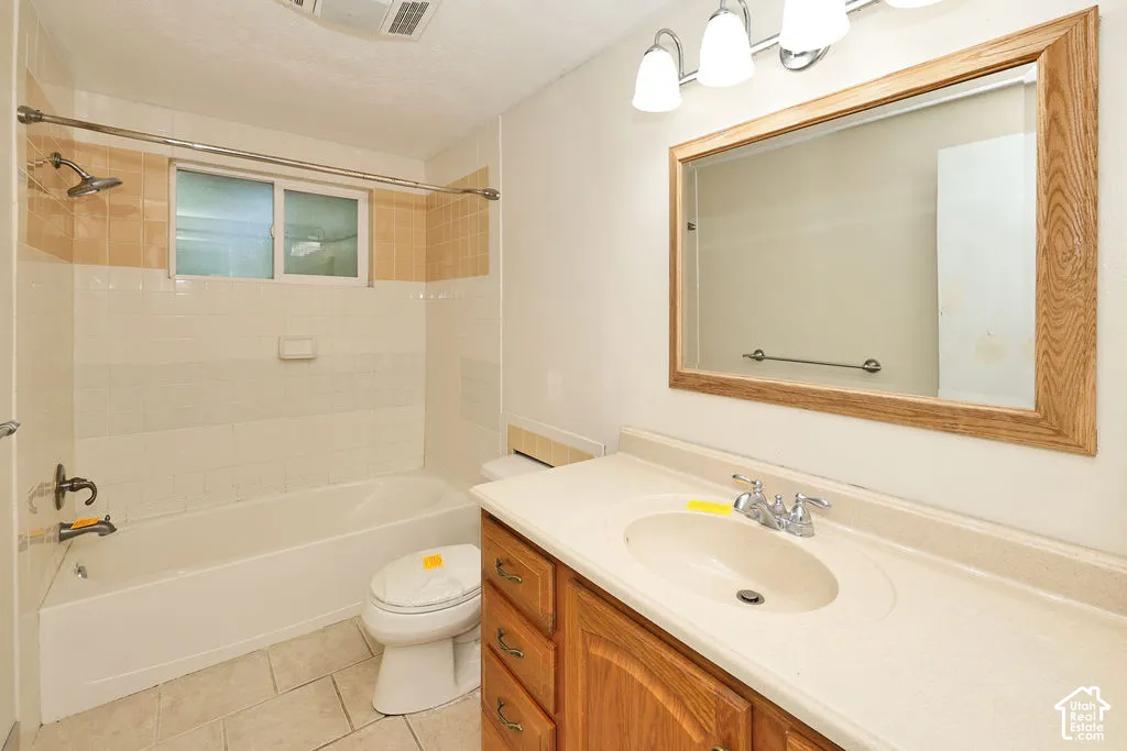 Light-toned tile flooring, built-in bathtub with shower, wood-finish vanity with countertop, framed mirror, and chrome fixtures