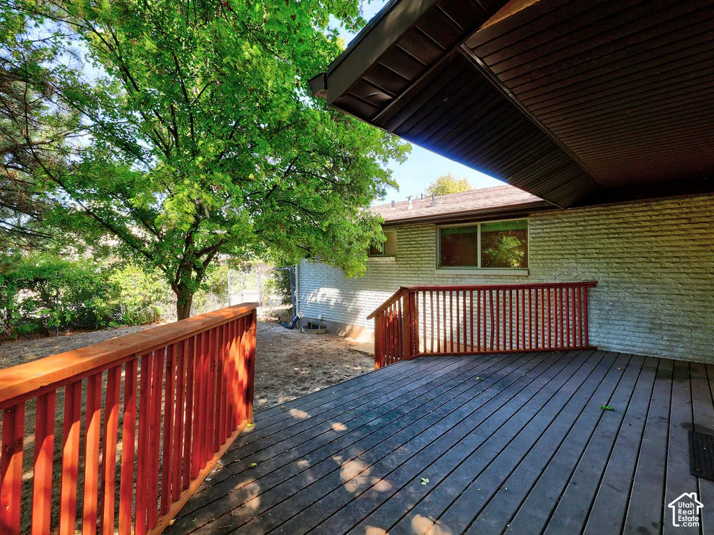 Spacious outdoor deck with a wood railing, leading to an expansive yard featuring mature trees and a brick-clad exterior