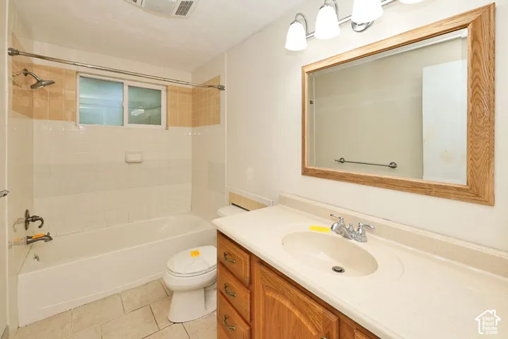 Light-toned tile flooring, built-in bathtub with shower, wood-finish vanity with countertop, framed mirror, and chrome fixtures