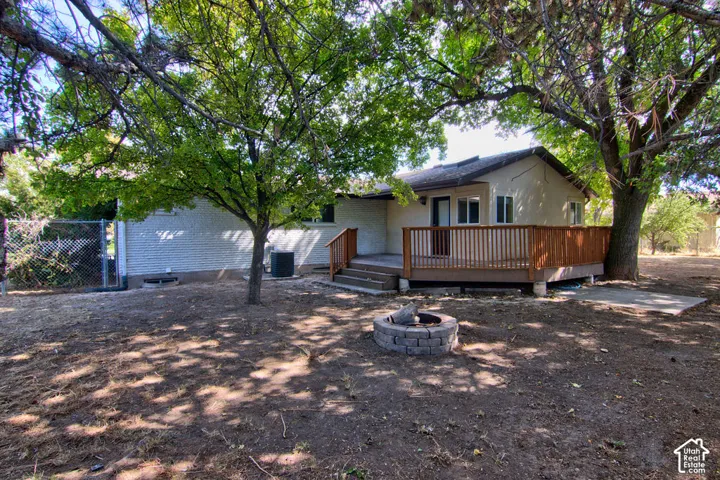 Expansive outdoor space featuring a wood-tone deck with railing, a stone-built fire pit, and mature shade trees