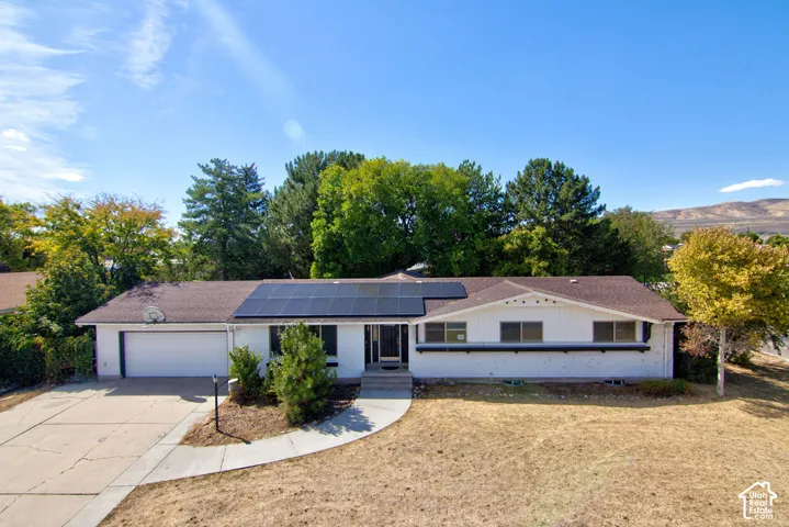 White exterior with dark roof, integrated solar panels, attached garage, and a concrete driveway