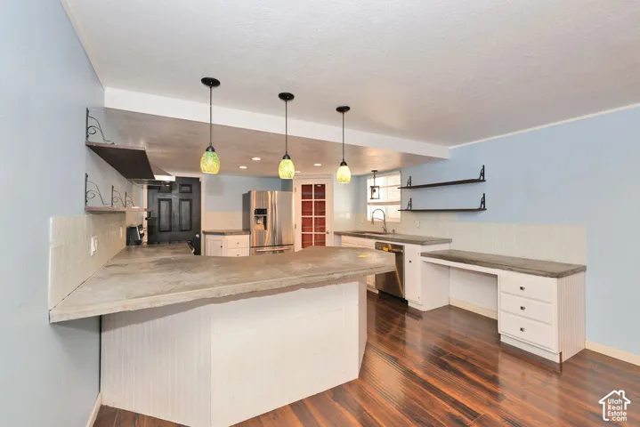 Kitchen featuring wood-finish flooring, white cabinetry, integrated stainless steel refrigerator, stainless steel dishwasher, and pendant lighting