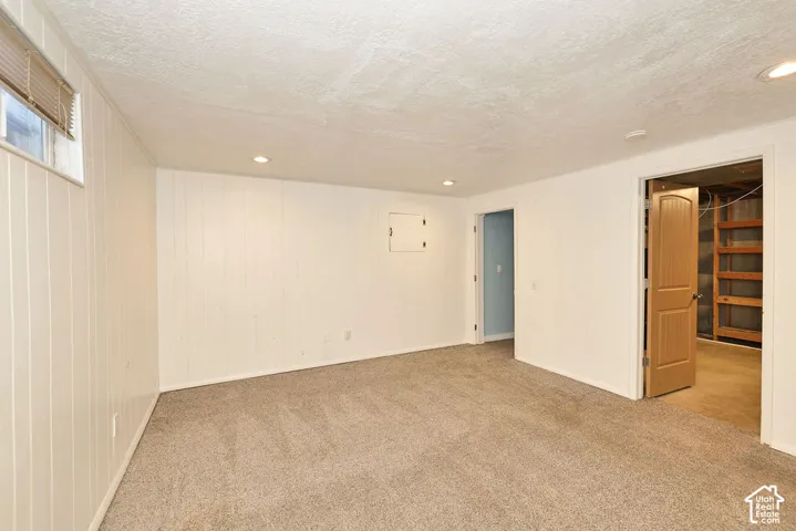 Carpet flooring, recessed lighting, white wall paneling, light wood-finish door, and additional room access