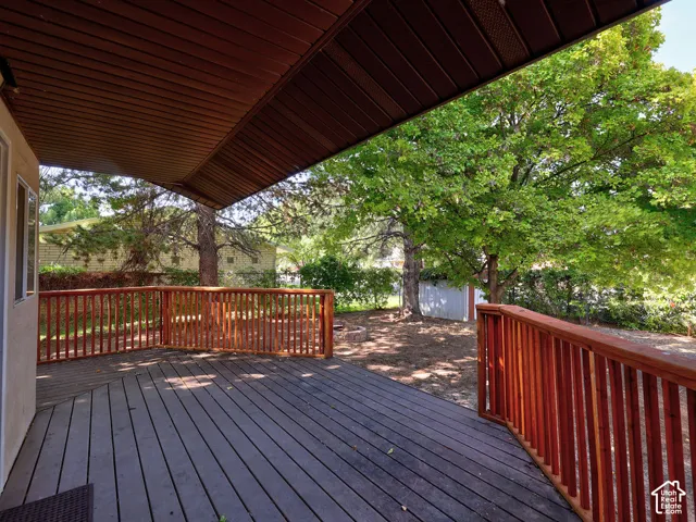 Covered outdoor deck with a wood-finish railing and mature trees
