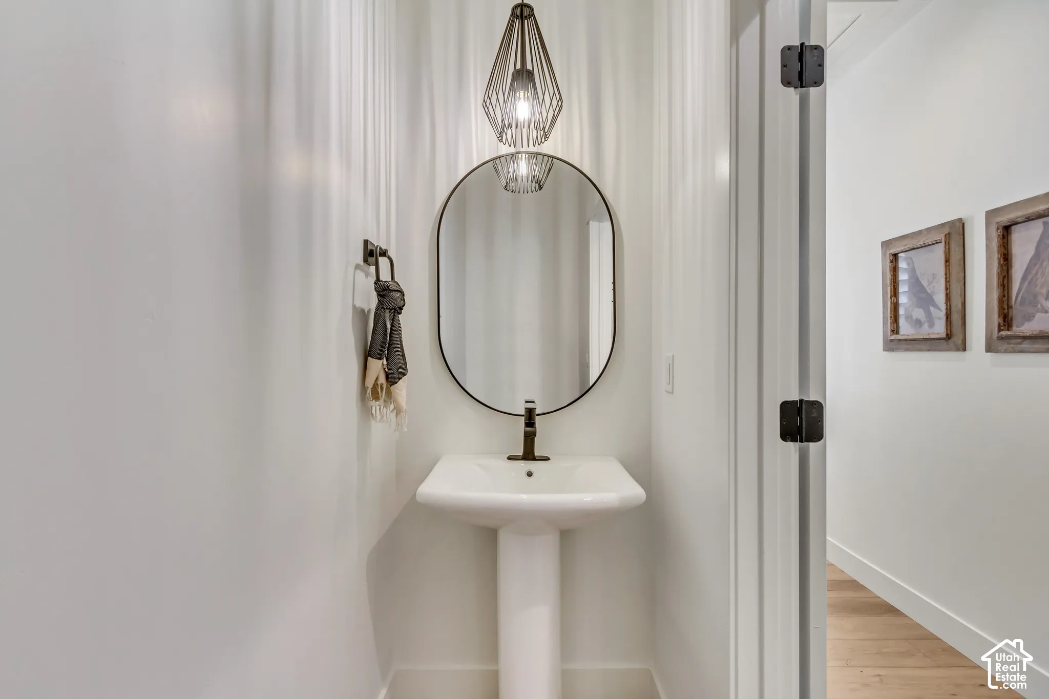 Pedestal sink with a dark bronze faucet, oval mirror, and a geometric pendant light fixture