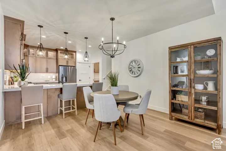 Expansive kitchen island with seating, stainless steel appliances, pendant lighting, wood-finish flooring, and a contemporary chandelier