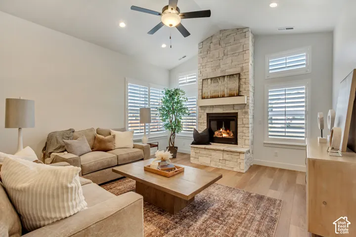 Vaulted ceilings with recessed lighting, stone-clad fireplace with mantel, wood-finish flooring, and white plantation shutters