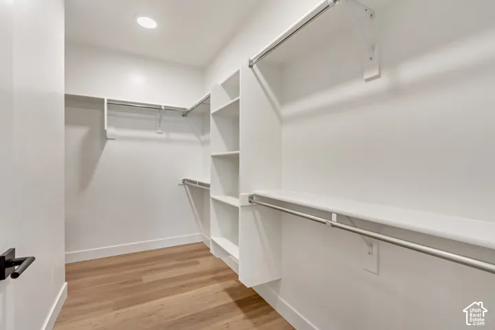 Walk-in closet featuring wood-finish flooring, recessed lighting, built-in shelving, and multiple hanging rods
