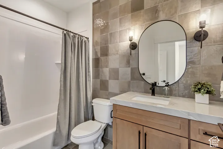 Built-in tub with shower, square wall tiles, light wood-finish vanity, white countertop with integrated sink, and black wall sconces
