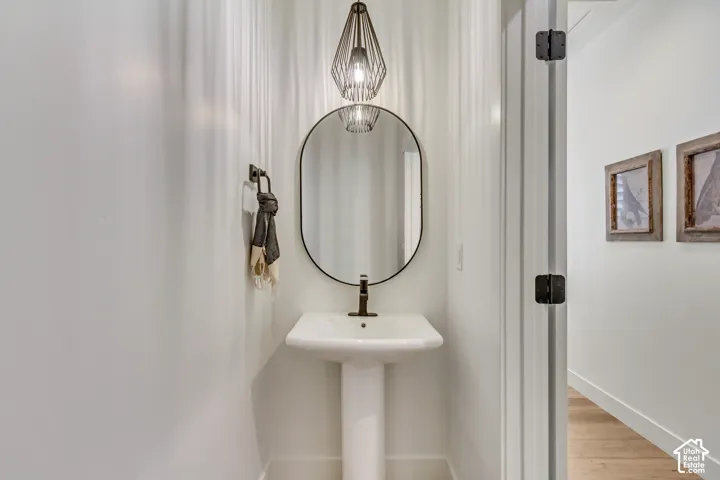 Pedestal sink with a dark bronze faucet, oval mirror, and a geometric pendant light fixture