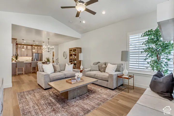 Vaulted ceiling with a ceiling fan, wide plank wood-finish flooring, white plantation shutters, and a built-in stone hearth