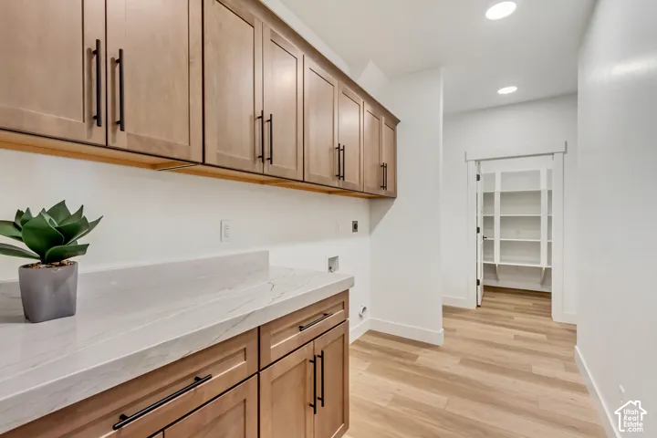 Extensive cabinetry with matte black hardware, light-toned wood-finish flooring, white walls, recessed lighting, and a walk-in pantry with built-in shelving