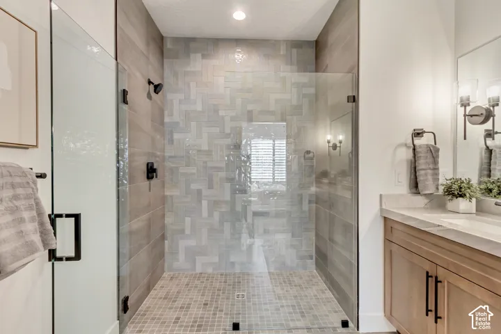 Glass-enclosed shower with a herringbone tile accent wall, coordinating mosaic tile floor, and matte black fixtures