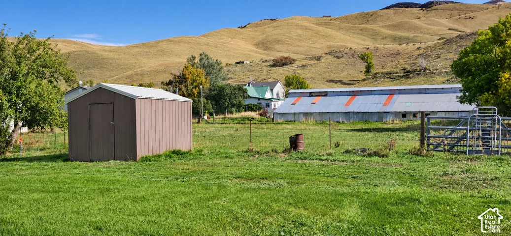 Expansive green space with a storage shed, barn structure, and rolling hills in the background