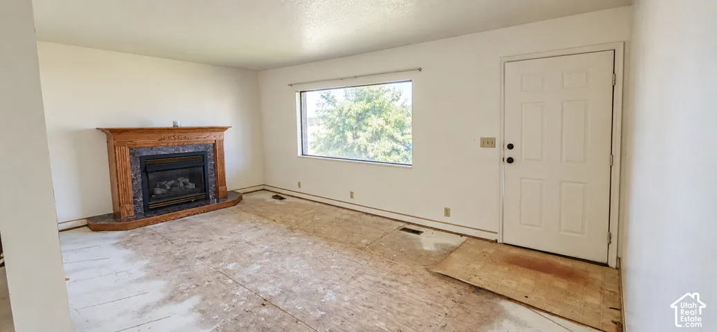 Living area featuring a wood-surround fireplace with a dark stone-tile inlay, a large picture window, and a paneled entry door