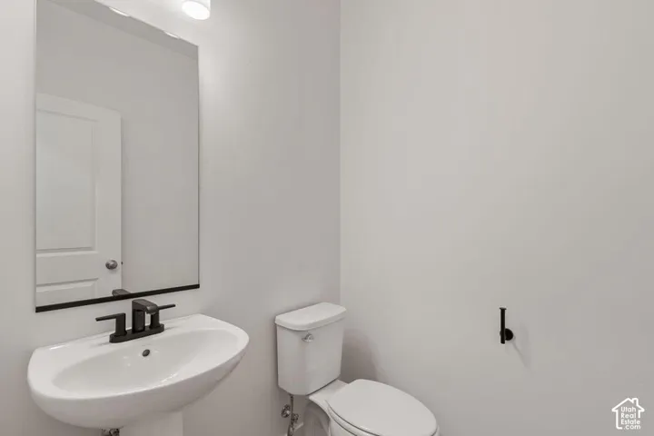 Pedestal sink with a matte black faucet, wall-mounted mirror, and toilet