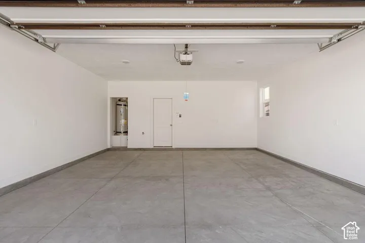 Spacious garage with a concrete floor, painted walls, a single window, and a built-in water heater alcove