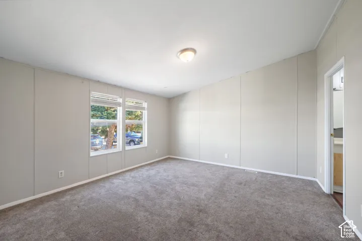 Neutral tone wall panels, two windows with blinds, gray carpet, and a flush mount ceiling light