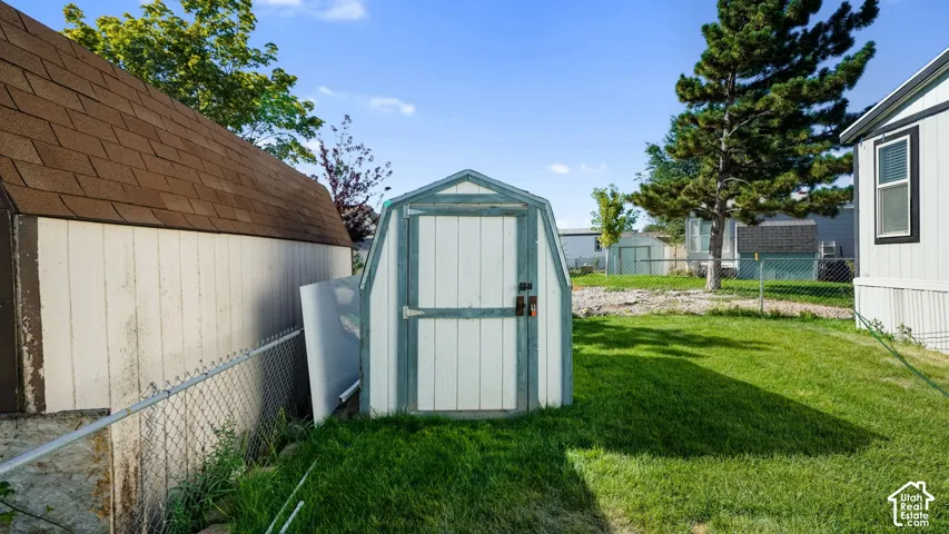 Two storage sheds, one with an arched roof and the other with a gambrel roof, are situated on a grassy area with a chain-link fence