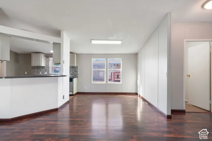 Spacious open-concept living area featuring wood-finish flooring, white walls, and a breakfast bar with a dark countertop