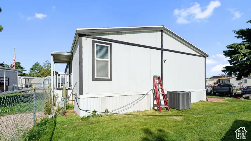 White siding exterior with a chain link fence, green lawn, and air conditioning unit