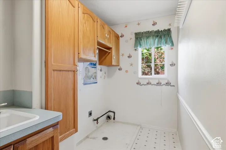 Utility space featuring wood-finish cabinetry, a white drop-in sink with a solid-surface countertop, tile flooring, and a single-pane window