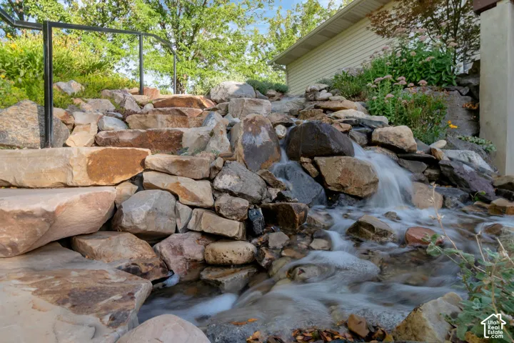 Stone stairway with a black metal handrail and a rock water feature. The waterfall feature continues on the other side of the stone stairway