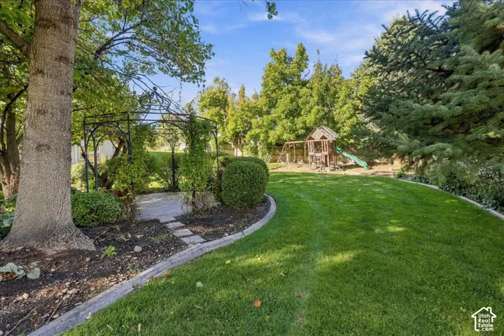 Expansive backyard featuring a wrought iron gazebo, stone paver pathway, manicured lawn, and mature trees