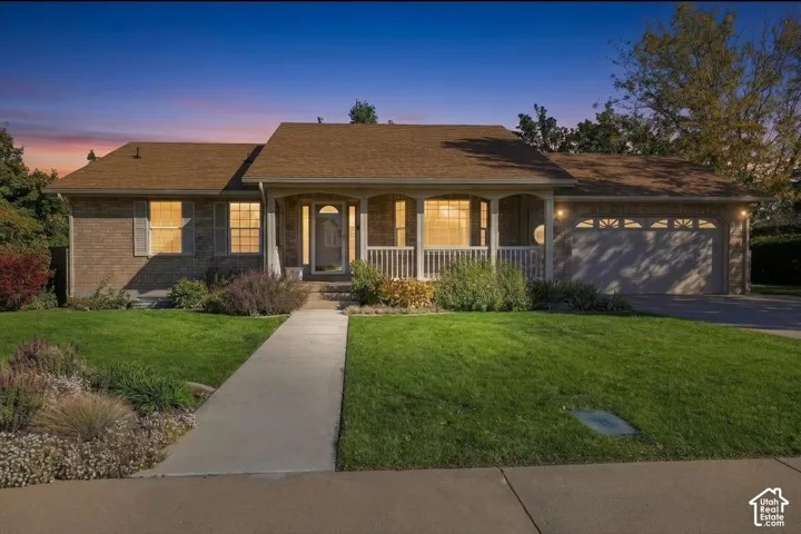 Brick exterior residence featuring a covered front porch, arched entryway, shingled roof, and an attached two-car garage