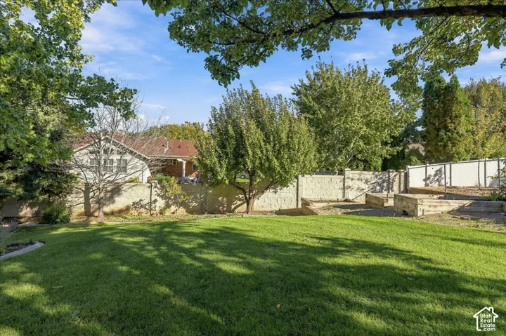 Expansive backyard featuring a grass lawn, mature trees, tiered stone retaining walls, and perimeter masonry fencing