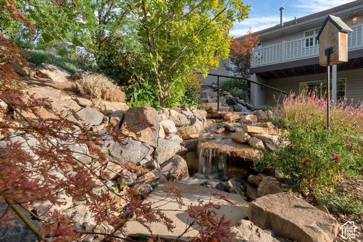 Tiered rock landscaping featuring a multi-level waterfall, established perennials, and a black metal railing along the steps