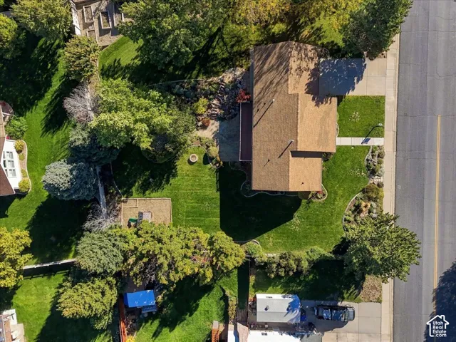 Aerial view of property featuring a large grass lawn, mature trees, landscaped garden beds, and a hardscaped fire pit area