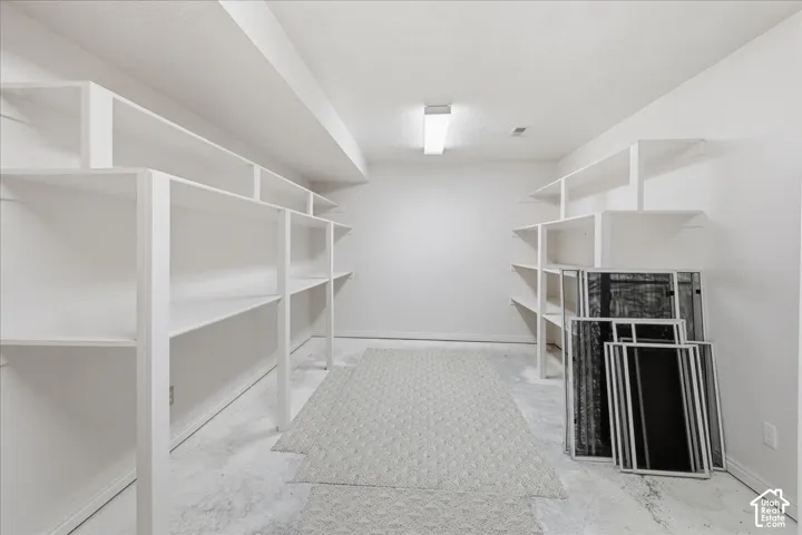 Storage room featuring white built-in shelving, concrete flooring, and an integrated ceiling light fixture