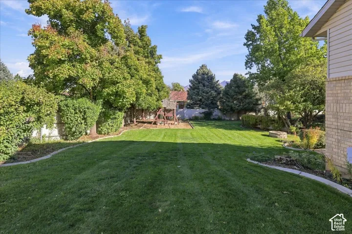 Backyard featuring a manicured lawn, perimeter landscape curbing, mature trees, and a circular stone fire pit