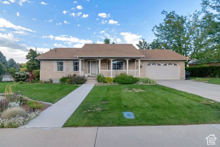 Brick exterior, covered front porch, attached garage, concrete driveway, and established landscaping