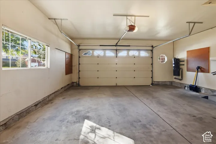 Tandem depth 2 car garage. featuring  inset windows on door, concrete flooring, side window, and built-in wall-mounted utility systems