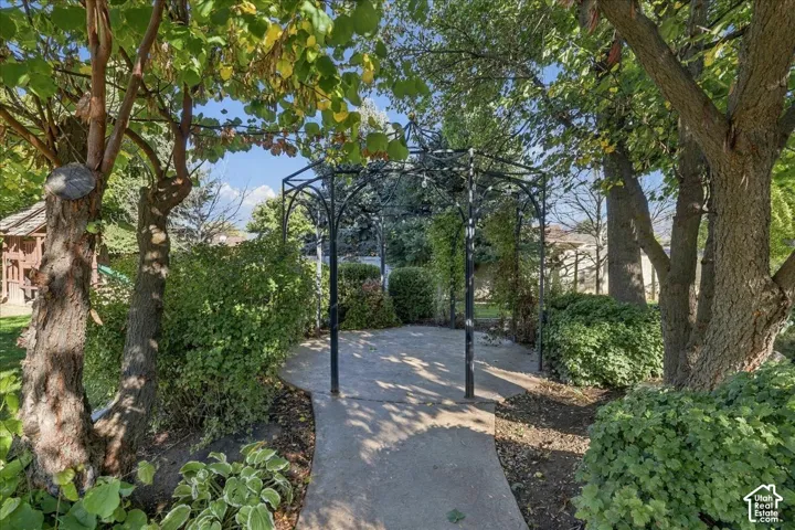 Backyard featuring a wrought-iron garden arbor, concrete hardscaping, mature trees, and established greenery