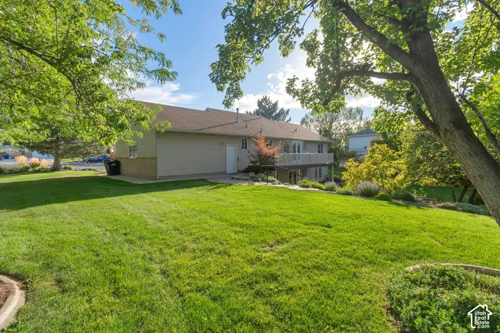 Expansive green lawn with mature trees and a rambler exterior featuring a balcony and lower-level patio